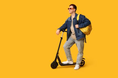 Sarı arka planda modern elektrikli scooter kullanan erkek öğrenci.