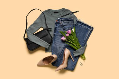 Gri uzun kollu kot, çanta, yüksek topuklu ayakkabı, şık saat ve bej arka planda lale çiçekleri.