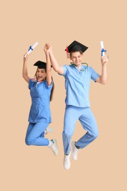 Bej duvarın yanında diploması ve steteskopu olan mutlu tıp mezunu bir çift.