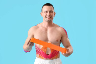 Mavi arka planda fizyo bandı olan genç kaslı adam.