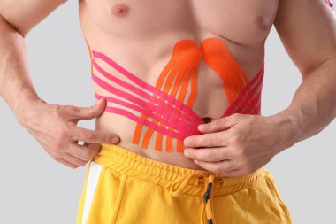 Young muscular man with physio tape on his abdomen against light background, closeup clipart