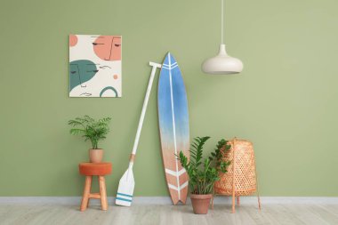 İçinde tahta sörf tahtası, bitki ve yeşil duvarın yanındaki resim olan ışık odasının içi.