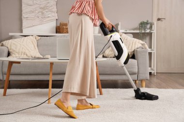 Young woman cleaning carpet with cordless stick vacuum cleaner in living room