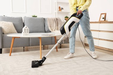 Young woman cleaning carpet with cordless stick vacuum cleaner in living room
