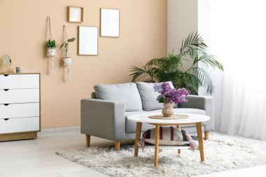 Gri kanepenin yanındaki sehpanın üzerinde bir demet leylak dalı olan oturma odasının içinde.