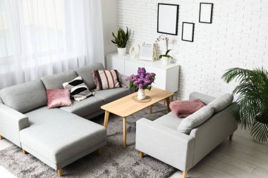 Gri kanepelerin yanındaki sehpanın üzerinde leylak dalları olan şık bir oturma odası.