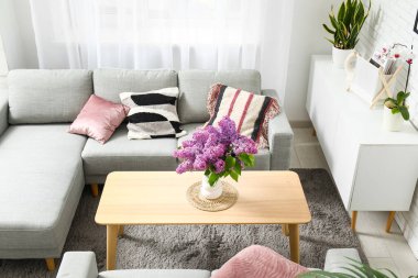 Gri kanepelerin yanındaki sehpanın üzerinde leylak dalları olan şık bir oturma odası.