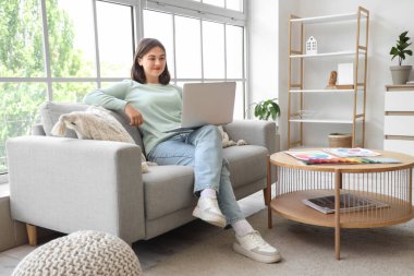 Evdeki kanepede dizüstü bilgisayarla çalışan kadın iç mimar.