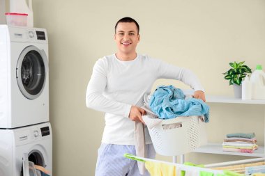 Çamaşır odasında kirli çamaşırlarla dolu sepeti tutan genç adam.