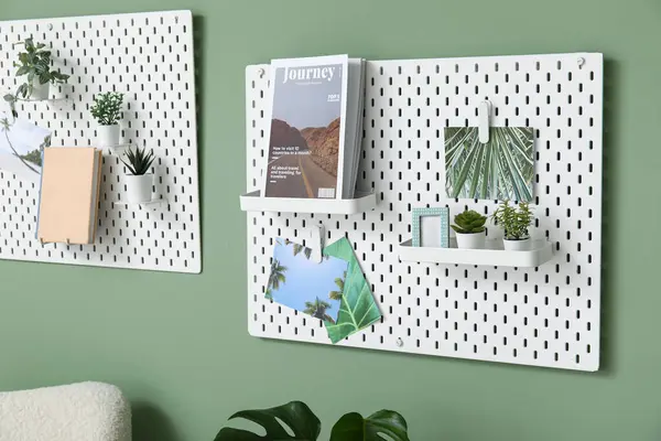 stock image Pegboards with magazines, pictures and houseplants on green wall in living room