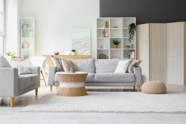 Oturma odasının içinde kanepeler, rattan masa ve yumuşak halı var.