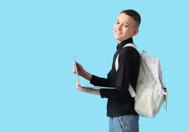 Mavi arka planda dizüstü bilgisayarı ve sırt çantası olan tatlı bir okul çocuğu.