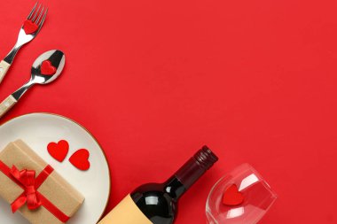 Kırmızı arka planda bir şişe şarap ve hediye kutusuyla güzel bir masa. Sevgililer Günü kutlaması