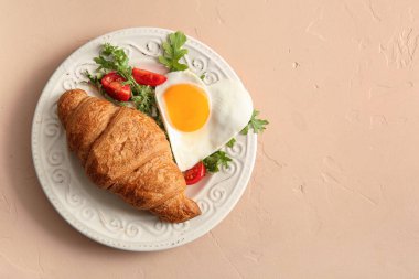 Lezzetli kızarmış yumurta, kruvasan, domates ve bej arkaplanda roka.