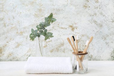 Bambu diş fırçası, temiz havlu ve arka planda okaliptüs dalı olan tutucu.