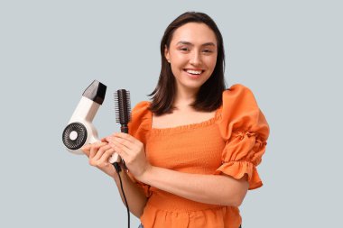 Saç kurutma makinesi ve arka planda fırçası olan güzel genç bir kadın.
