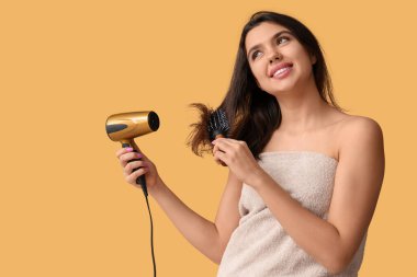 Havlu, saç kurutma makinesi ve sarı arka planda fırçası olan genç ve güzel bir kadın.