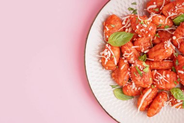 Pembe arka planda peynirli bir tabak lezzetli gnocchi.