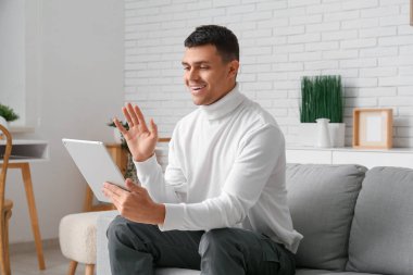 Tablet bilgisayarlı yakışıklı genç adam evde online randevuda görüntülü sohbet ediyor.