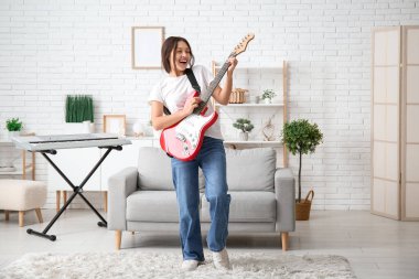 Elektro gitar çalıp evde şarkı söyleyen genç bir kadın.