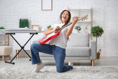 Elektro gitar çalıp evde şarkı söyleyen genç bir kadın.