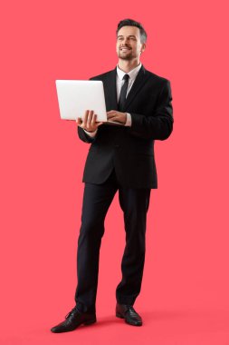 Kırmızı arka planda dizüstü bilgisayarı olan erkek işadamının portresi