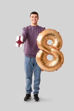 Yakışıklı adam balonu 8 şeklinde tutuyor ve beyaz arka planda hediye kutusu var.