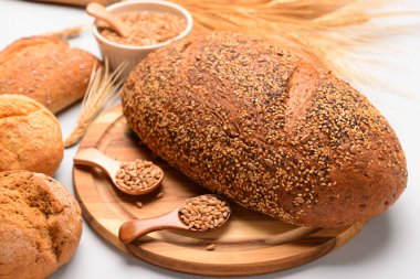 Tahta tahta tahta somun taze ekmek, çörekler, kaşıklar ve beyaz arka planda buğday taneleri.