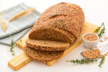 Beyaz arka planda dilimlenmiş somun ekmek, buğday dikenleri, tahıllar ve kekik ile ahşap tahta.