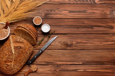 Tahta zemin üzerinde dilimlenmiş somun ekmek, buğday dikenleri, tahıllar ve kekik.