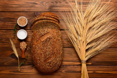 Tahta zemin üzerinde dilimlenmiş somun ekmek, buğday dikenleri, tahıllar ve kekik.
