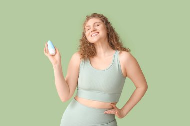 Yeşil arka planda deodorantı olan mutlu genç bir kadın.