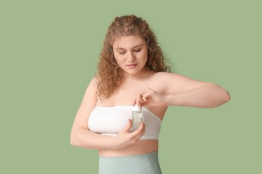 Yeşil arka planda deodorantı olan güzel genç bir kadın.