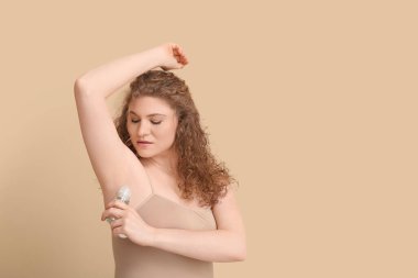 Bej arka plana deodorant süren güzel genç bir kadın.