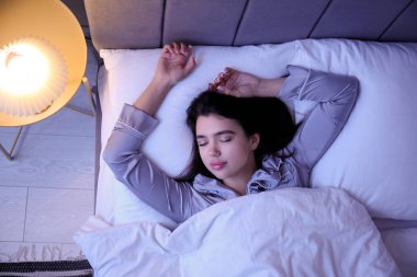 Beautiful young woman sleeping in bedroom at night, top view