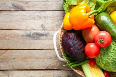 Gri ahşap arka planda farklı taze sebzelerle hasır sepet.