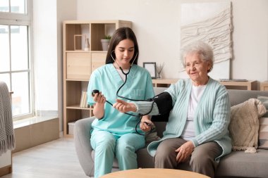 Evde yaşlı bir kadının kan basıncını ölçen genç bir bakıcı.