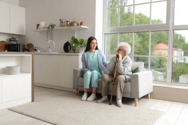 Genç bakıcı ve yaşlı kadın mutfaktaki kanepede oturuyor.