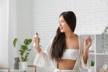 Güzel, genç, mutlu bir kadın evde saç spreyi sıkıyor.