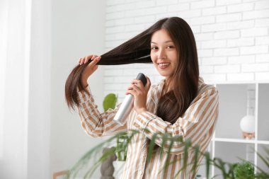 Güzel, genç, mutlu bir kadın evde saç spreyi sıkıyor.