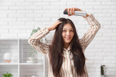 Güzel, genç, mutlu bir kadın evde saç spreyi sıkıyor.