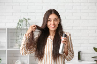 Güzel, genç, mutlu bir kadın evde saç spreyi sıkıyor.