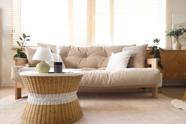 Oturma odasındaki masada dizüstü bilgisayarı ve lambası olan hava nemlendirici.