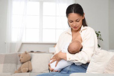 Annem bebeğini evdeki kanepede emziriyor.