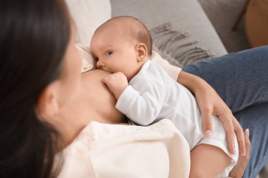 Anne bebeğini evdeki kanepede emziriyor.