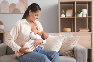 Annem bebeğini evdeki kanepede emziriyor.