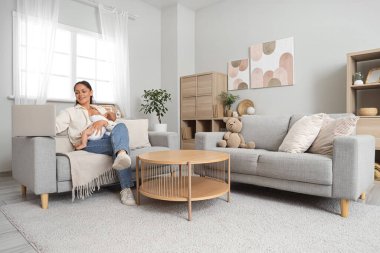 Annem evdeki kanepede dizüstü bilgisayar kullanırken bebeğini emziriyor.