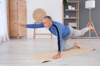 Sportif olgun bir adam evde yoga yapıyor.