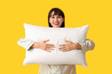 Sarı arka planda yumuşak yastıklı pijamalı mutlu genç kadın.