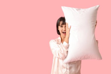 Pembe arka planda yumuşak yastıklı pijamalı güzel bir kadın.